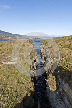 A serene natural landscape with a narrow water channel leading to a larger body of water under a clear sky
