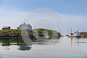 A serene Norwegian landscape, with Rorbu cabins and a docked fishing vessel mirrored on the tranquil waters of Lofoten. Norway