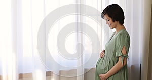 Serene peaceful pregnant woman hold hands on belly standing indoor