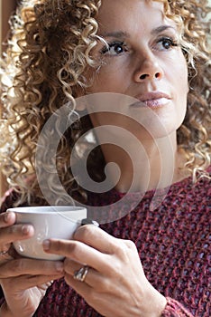 Serene people concept lifestyle. One woman drinking coffee or healthy beverage tea alone ner the window at home looking outside