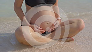 A serene pregnant woman is sitting on a pristine beach, with the gentle sea breeze complementing the close-up view of