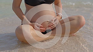 A serene pregnant woman is sitting on a pristine beach, with the gentle sea breeze complementing the close-up view of