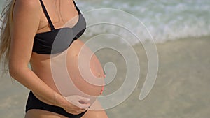 A serene pregnant woman is walking on a pristine beach, with the gentle sea breeze complementing the close-up view of