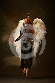 Serene redhead woman with white wings and halo, floating in old-fashioned chainmail top and black skirt against vintage