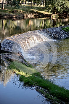 A serene river scene featuring a small stone dam with water gently cascading over the edge photo