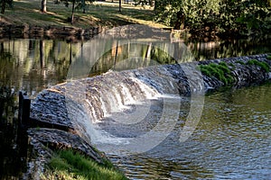 A serene river scene featuring a small stone dam with water gently cascading over the edge photo