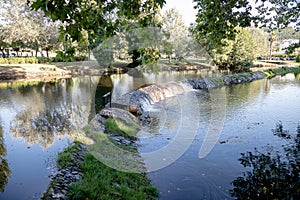 A serene river scene featuring a small stone dam with water gently cascading over the edge photo
