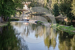 A serene river scene featuring a small stone dam with water gently cascading over the edge photo