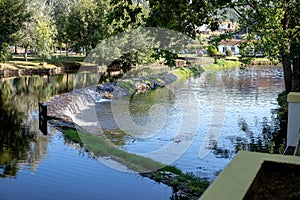 A serene river scene featuring a small stone dam with water gently cascading over the edge photo