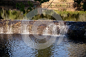 A serene river scene featuring a small stone dam with water gently cascading over the edge photo