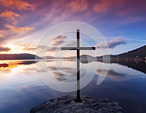 A serene scene of a cross standing on a calm lake with a beautiful sky background