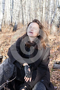 A serene scene of a young woman in a black coat sitting on a birch log in the autumn forest, surrounded by colorful fallen leaves