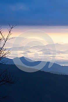 Serene scenery of blue mountain range in the morning mist, a village and a river in the misty valley