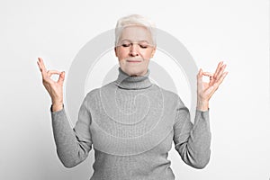 Serene senior lady with meditative pose on grey background