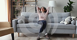 Serene smiling woman chilling, dreaming on sofa hands behind head