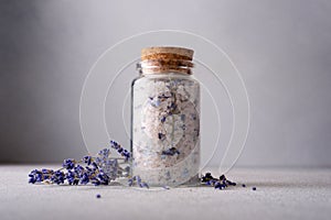 A serene spa setting with a glass jar of aromatic lavender salt sealed with a cork, surrounded by scattered lavender flowers,