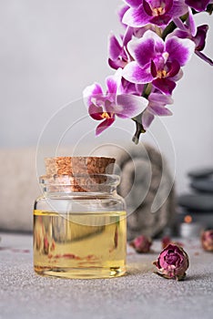 A serene spa still life featuring essential oils, smooth pebbles, a rolled grey towel, and a vibrant purple orchid