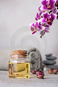 A serene spa still life featuring essential oils, smooth pebbles, a rolled grey towel, and a vibrant purple orchid