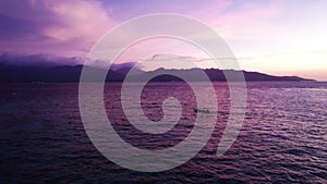 Serene sunset over the sea with a boat and mountain silhouette aerial drone shot