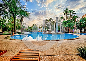 Serene Sunset at a Resort Pool Surrounded by Lush Greenery and Classical Columns