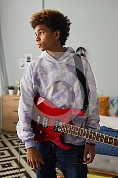 Serene teenage guy with electric guitar hanging on his shoulder