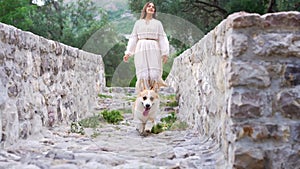 A serene walk, woman and Pembroke Welsh Corgi on ancient bridge, surrounded by lush trees