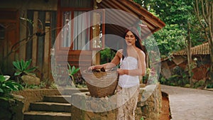 Serene woman holding a basket near a rustic cabin surrounded by lush greenery