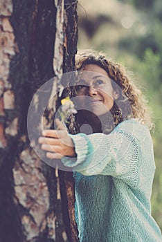 Serene woman hugging tree trunk in the forest smiling and looking at the woods around. People in love for nature. Outdoors
