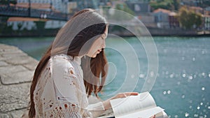 Serene woman looking book turning pages beautiful river promenade. Lady reading