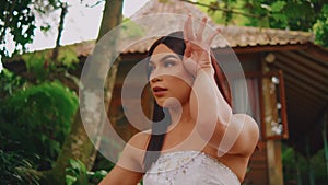 Serene woman in a white dress enjoying nature in a lush garden, with a peaceful expression and closed eyes