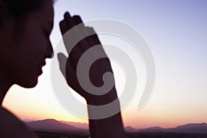 Serene young woman with eyes closed and hands together in prayer pose in the desert in China, focus on background