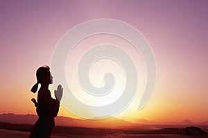 Serene young woman with hands together in prayer pose in the desert in China, silhouette, profile, sun setting