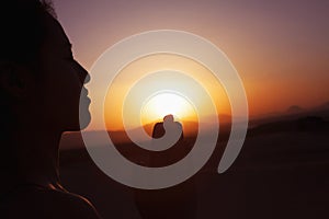 Serene young woman with hands together in prayer pose in the desert in China, silhouette, sun setting