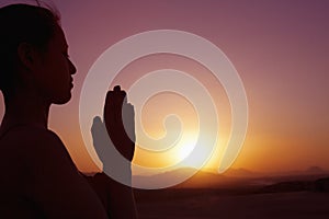 Serene young woman with hands together in prayer pose in the desert in China, silhouette, sun setting, profile