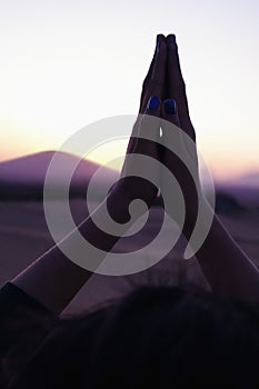 Serene young woman with her palms together in prayer held above her head in the desert in China, close-up