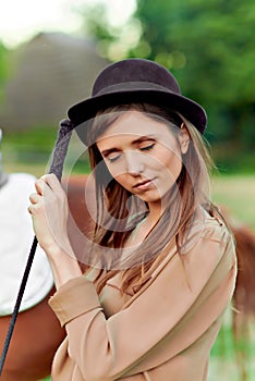 A serene young woman near a horse in the backdrop while keeping her eyes closed in a portrait. Wellness, calmness concept. posing