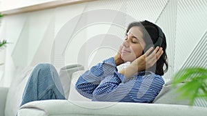 Serene young woman relaxing on comfortable sofa with eyes closed wearing headphones.