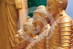 Series of Buddha statues. Face in the foreground, yellow gold sculptures.