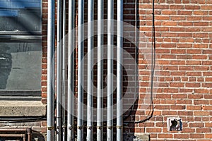 A series of metal conduits running parallel up and down the exterior wall of an old brick building photo