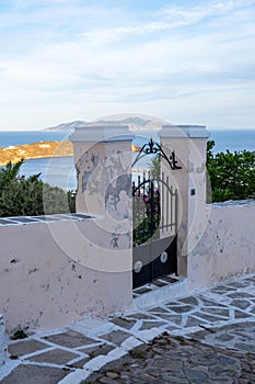 Serifos Island, Cyclades. House entrance gate closed, white fence, paved alley and sea view, Chora