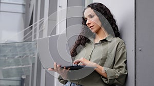 Serious 30s Latin Hispanic woman professional businesswoman standing near office building outdoors talking remote with