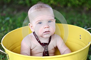 Serious 7-month-old white baby in yellow bucket