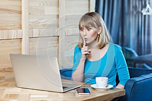 Serious adorable woman working on laptop, has video call, showing shh gesture.