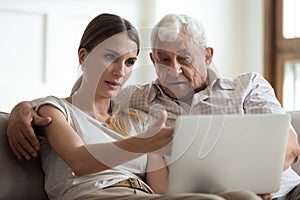 Serious adult daughter helping older father with laptop close up