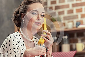 serious adult housewife talking by vintage wired phone and looking at camera