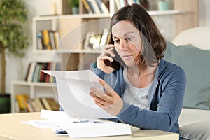 Serious adult woman checking letter calling on phone at home