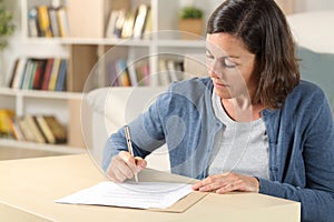 Serious adult woman signing document at home