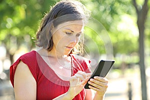 Serious adult woman using phone in a park