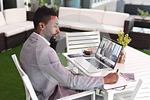 Serious african american businessman writing in diary while video conferencing over laptop in office