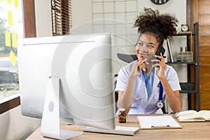Serious African American doctor working in her office at clinic in white medical gown and stethoscope busy working on computer